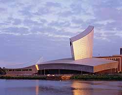 a photgraph of alarge modern building with an anvil like shape next to a stretch of water